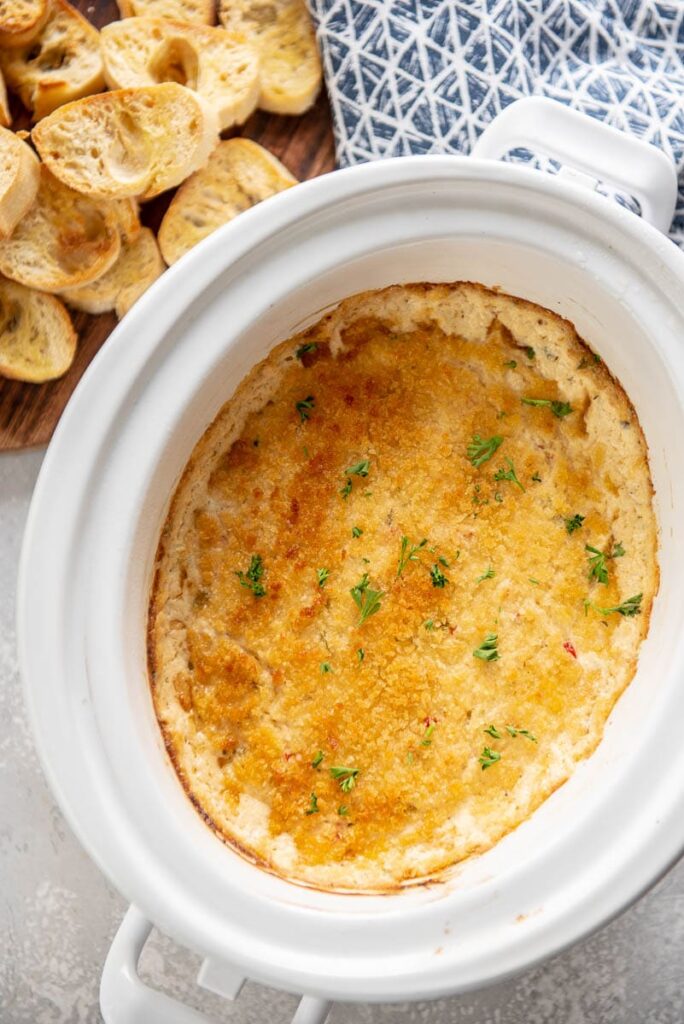 slow cooker filled with toasted crab dip with a side of bread