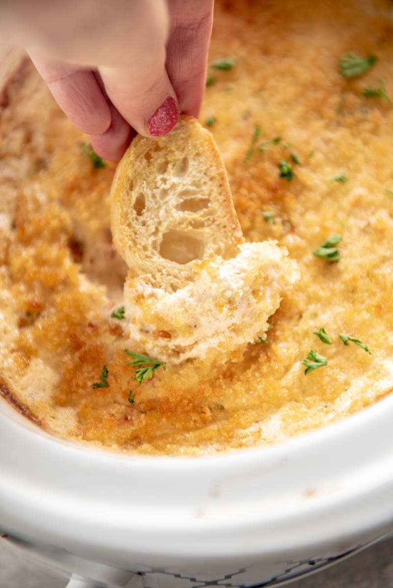 dipping bread into crab dip in slow cooker