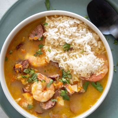 overhead view of shrimp and sausage gumbo in white bowl on green plate