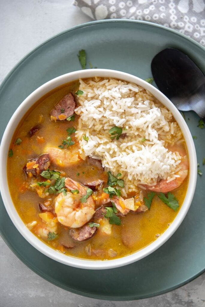 overhead view of shrimp and sausage gumbo in white bowl on green plate