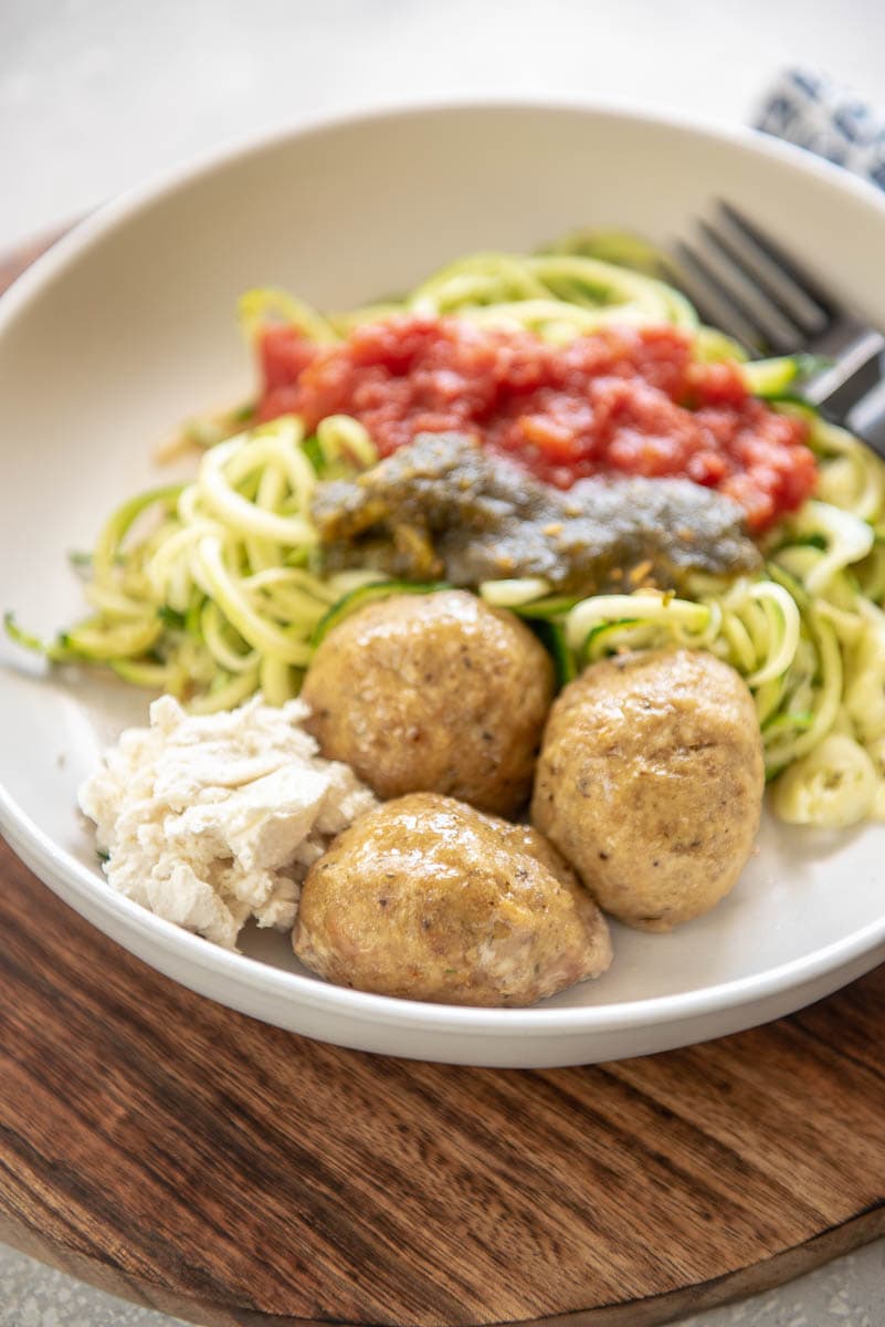 turkey meatballs on a white plate with noodles, marinara, and pesto