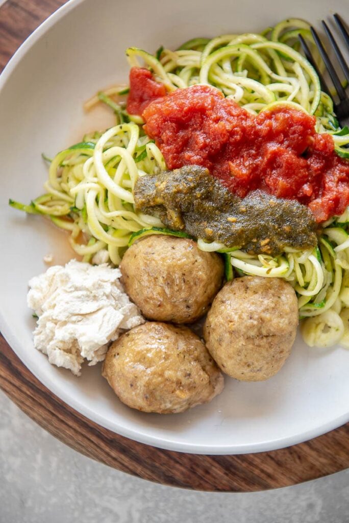turkey meatballs on a plate with zucchini noodles, marinara, and pesto