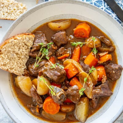 slow cooker beef bourguignon in a white bowl with bread and a spoon