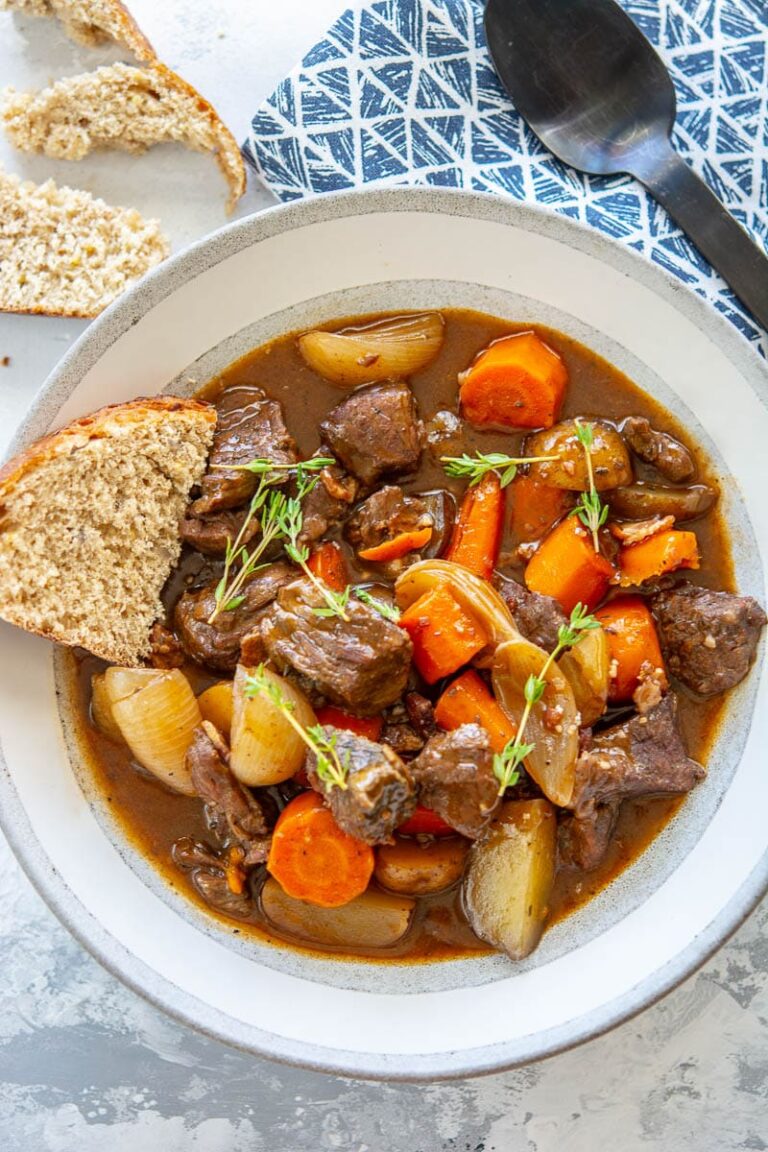 slow cooker beef bourguignon in a white bowl with bread and a spoon