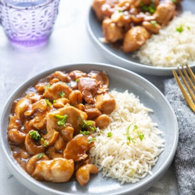 cashew chicken with rice on two plates with a glass of water