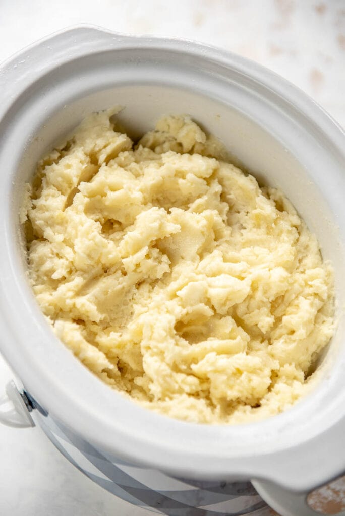 white slow cooker filled with cooked mashed potatoes