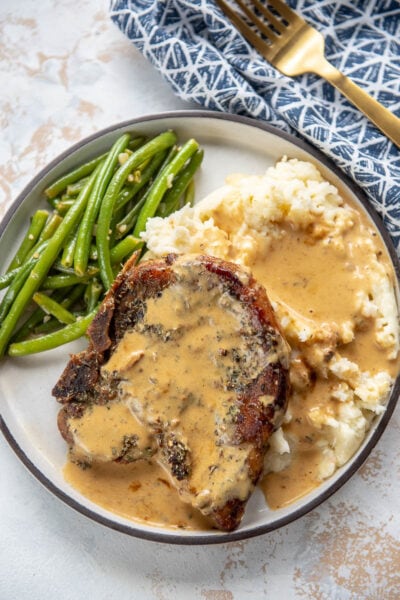 pork chop with mashed potatoes and green beans on a white plate topped with gravy