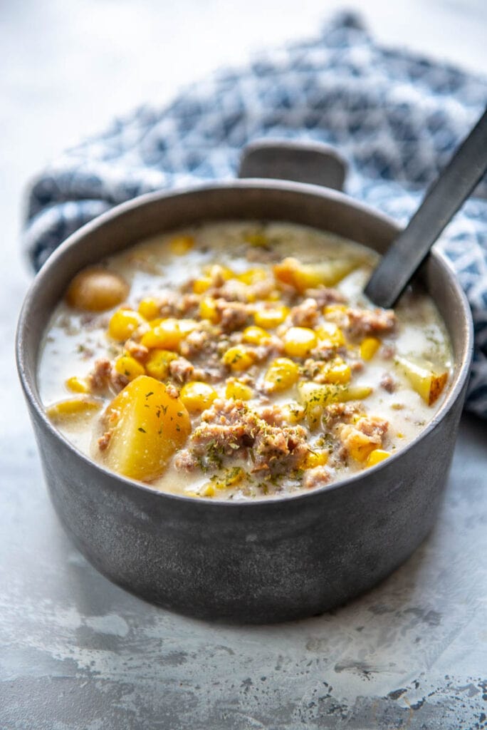 metal bowl filled with sausage potato and corn soup and black spoon