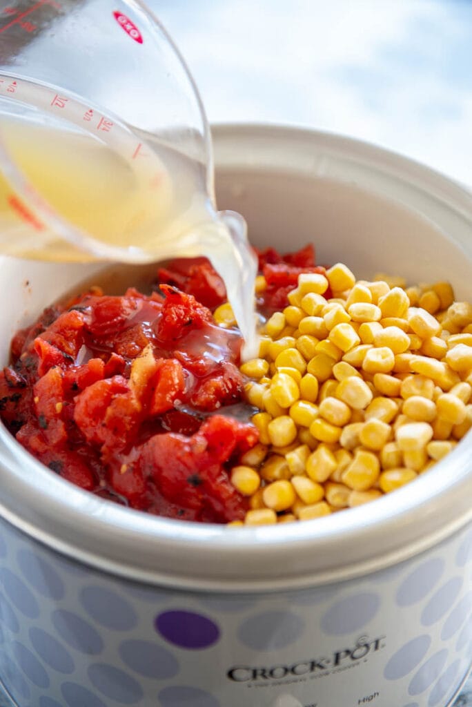 pouring broth over tomatoes and corn in slow cooker