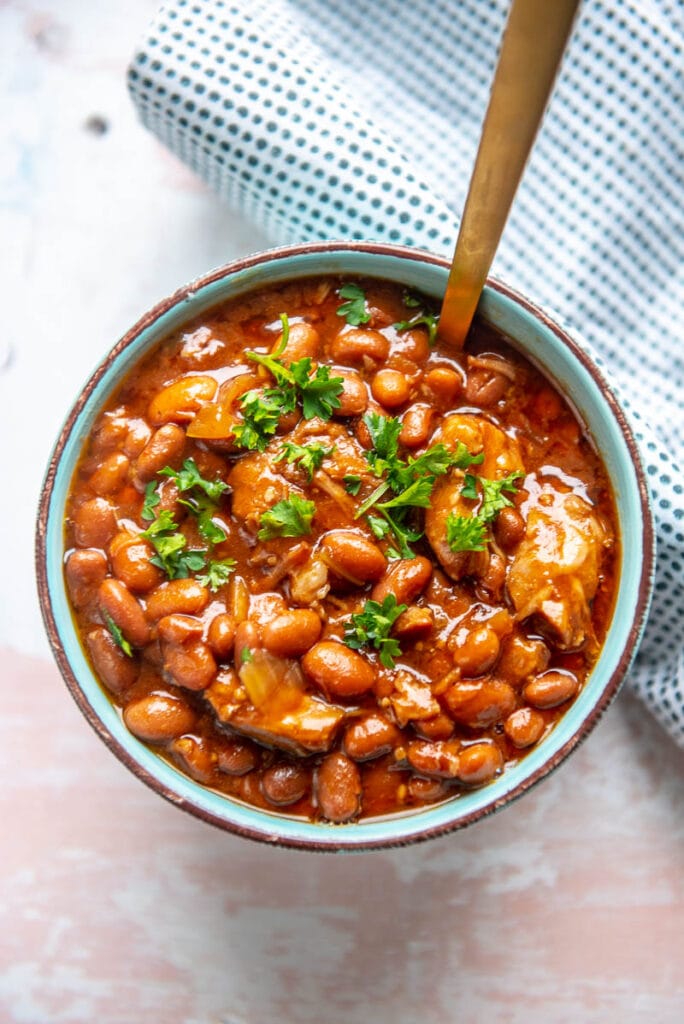 overhead shot of slow cooker pork and beans in a bowl with a spoon