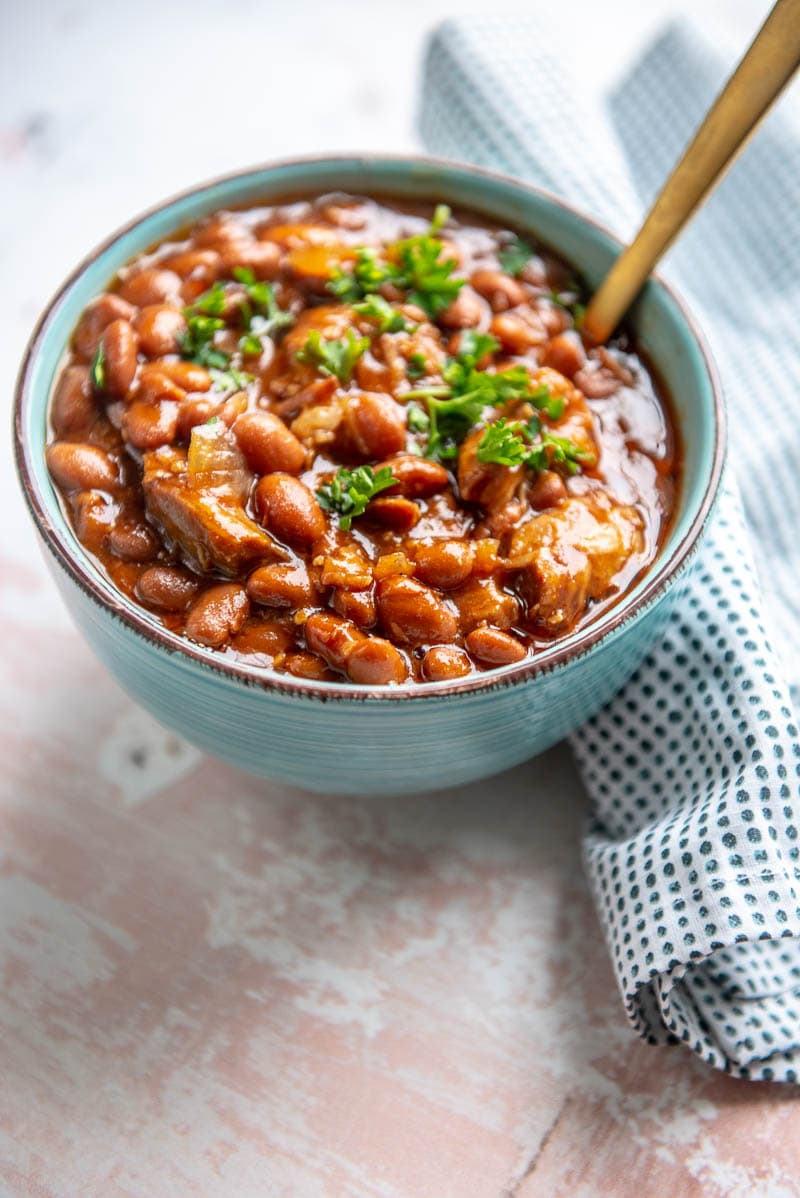 slow cooker pork and beans in a bowl with a spoon