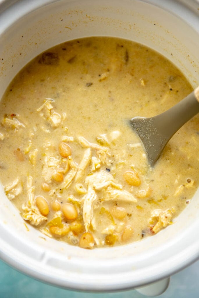 white chicken chili with shredded chicken in slow cooker with spoon