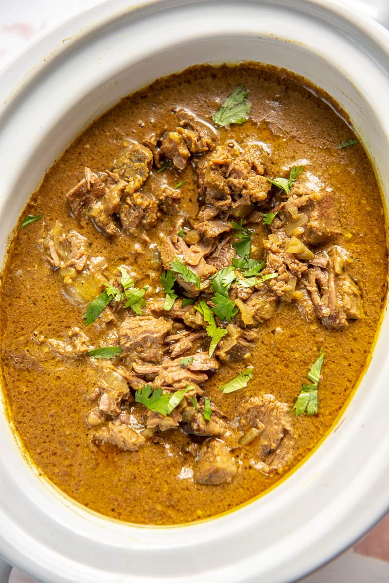 white oval slow cooker filled with flavorful beef curry