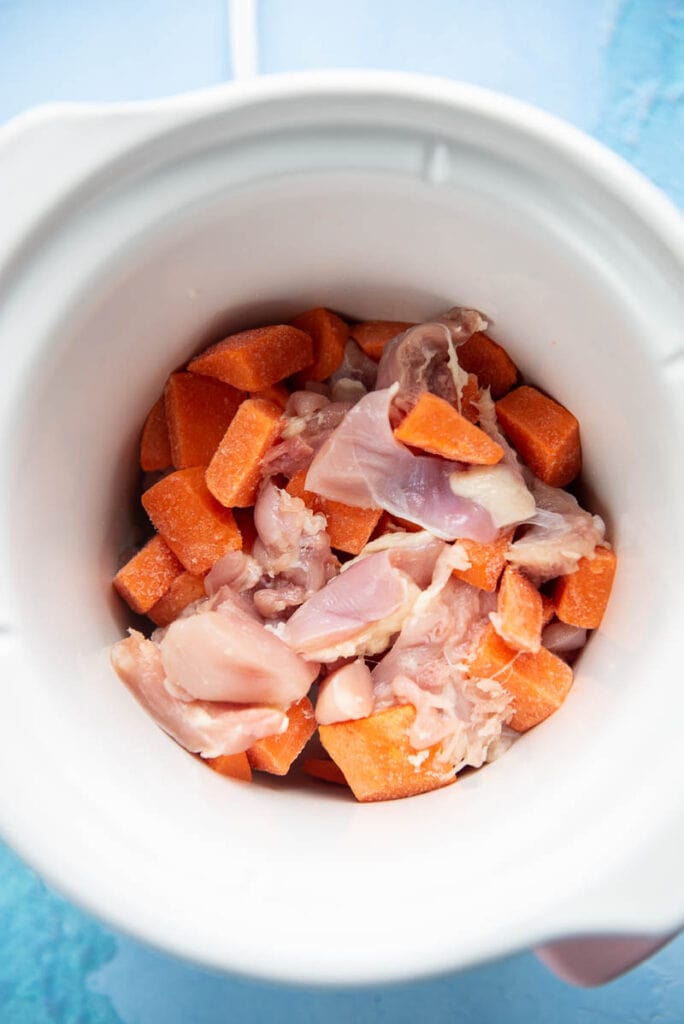 small white slow cooker filled with raw chopped chicken and sweet poatoes