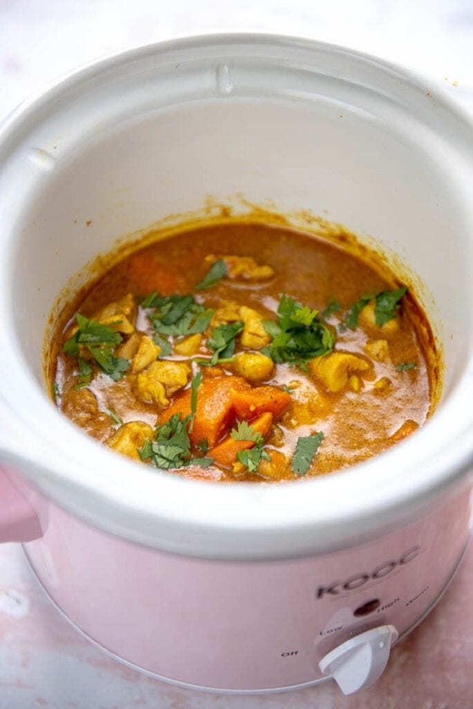 pink slow cooker filled with golden chicken korma