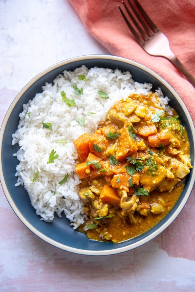 shallow blue bowl filled with rice and chicken korma with sweet potatoes