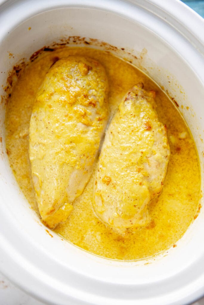 two cooked chicken breasts and honey mustard sauce in a slow cooker