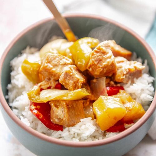 sweet and sour pork over rice in a bowl with spoon