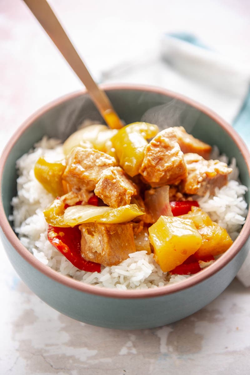 sweet and sour pork over rice in a bowl with spoon