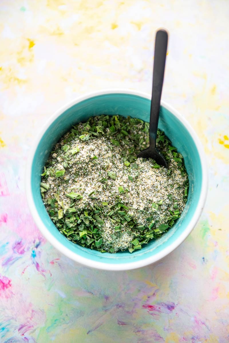 blue bowl filled with seasonings for ranch mix and tiny black spoon