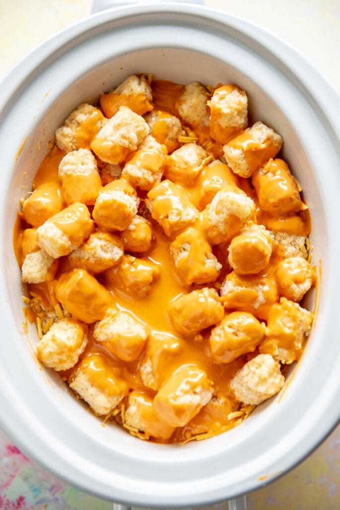 white slow cooker with tater tots topped with buffalo sauce