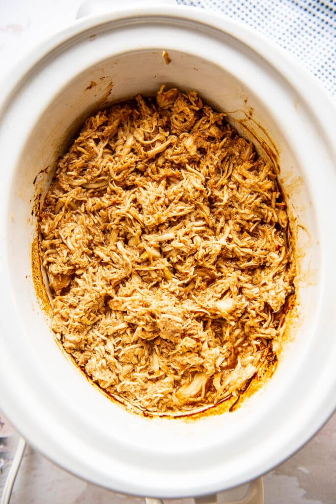 white slow cooker filled with bbq shredded chicken