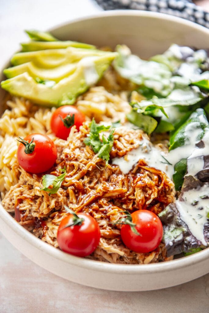 shredded bbq chicken in bowl topped with tomatoes, avocado and ranch