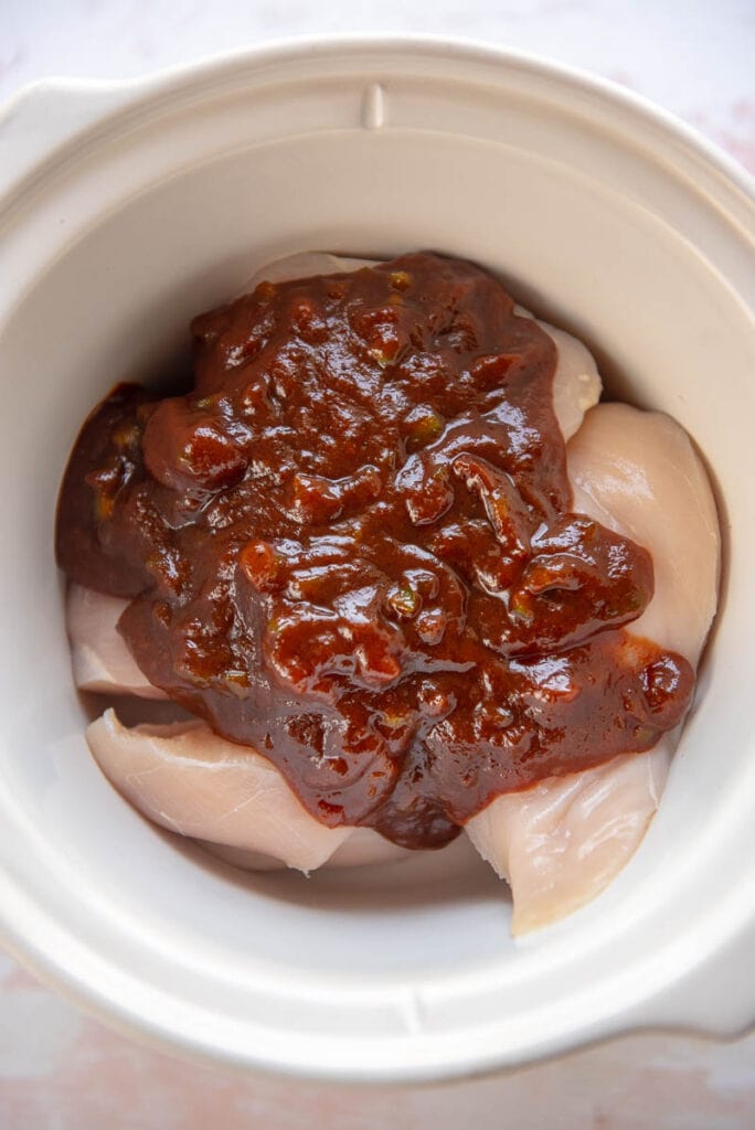 chicken breasts topped with bbq sauce in a round white slow cooker