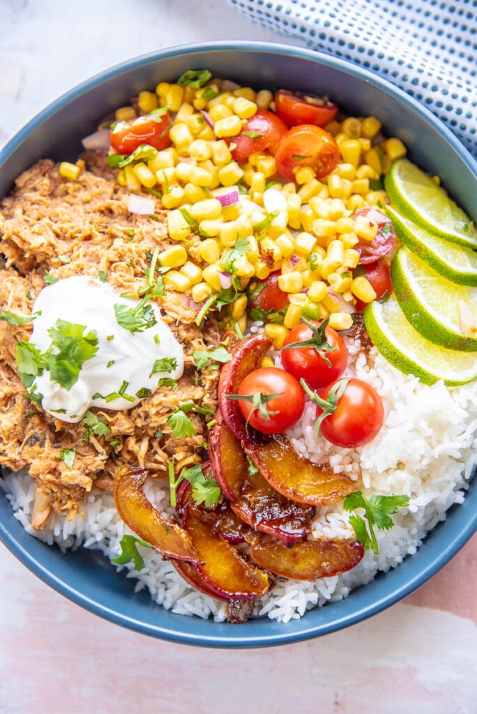shredded chicken, peaches and corn salsa on a bed of rice in blue bowl
