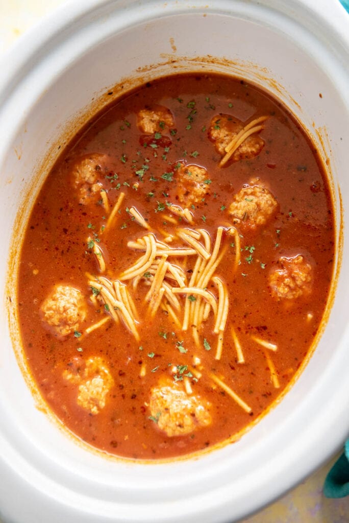 spaghetti and meatball soup in oval white slow cooker