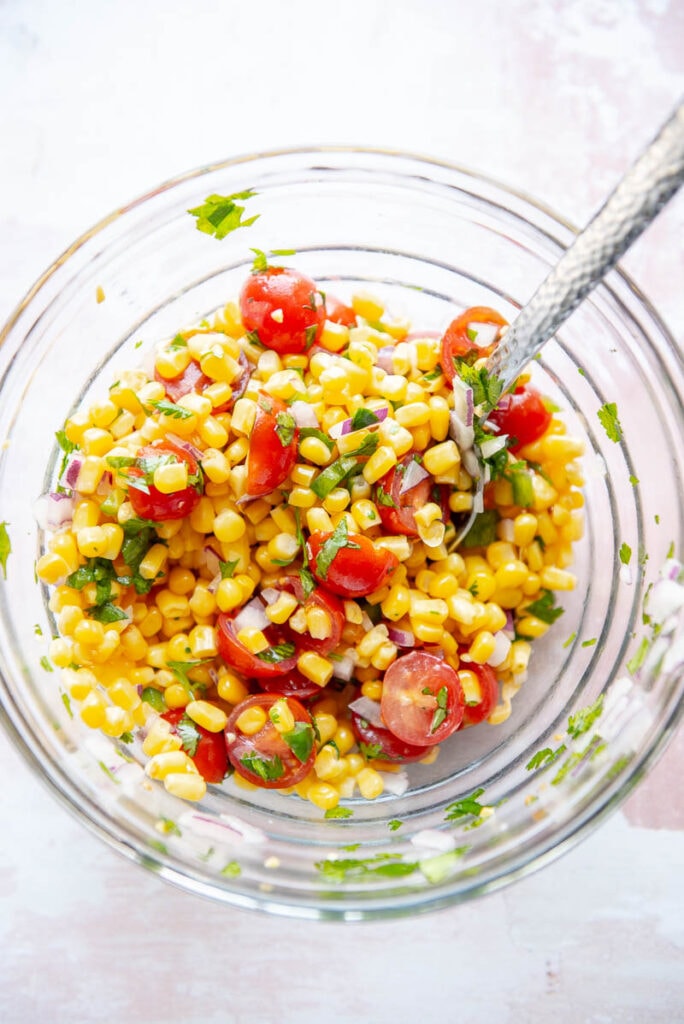 ingredients for tomato corn salsa in a glass bowl with spoon