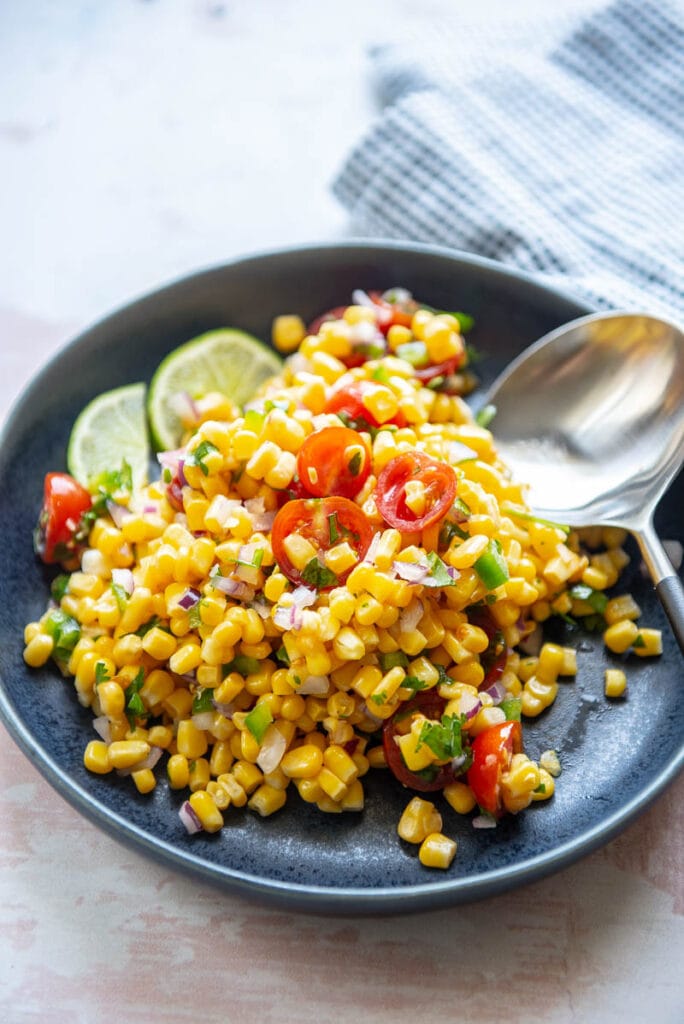 tomato corn salsa on a plate with spoon and lime garnish
