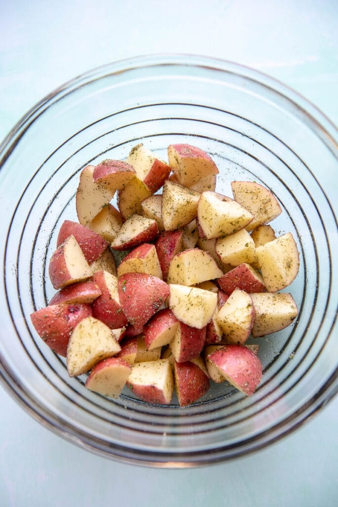 glass bowl filled with diced potatoes and sprinkled with seasoning