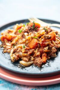 stack of pink and blue plates with beef and cabbage and carrot casserole on top