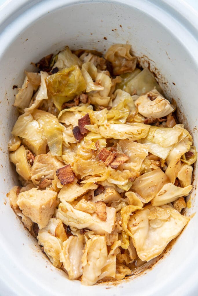 cooked cabbage with bacon and mustard in white oval slow cooker liner
