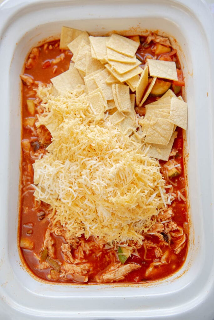 enchilada filling topped with chopped tortillas and shredded cheese in white dish