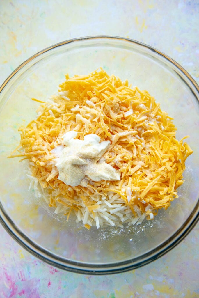 glass bowl filled with hash browns topped with cheese and sour cream
