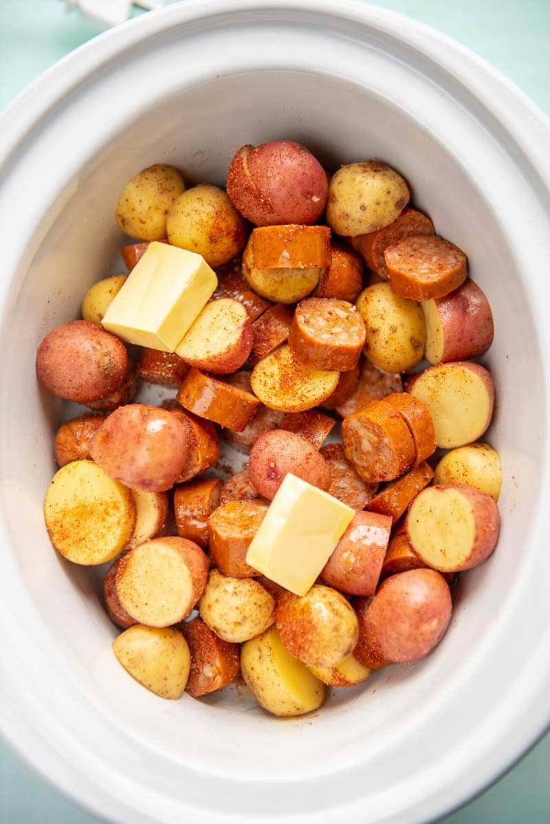 sliced potatoes, sausage and butter with seasonings in slow cooker