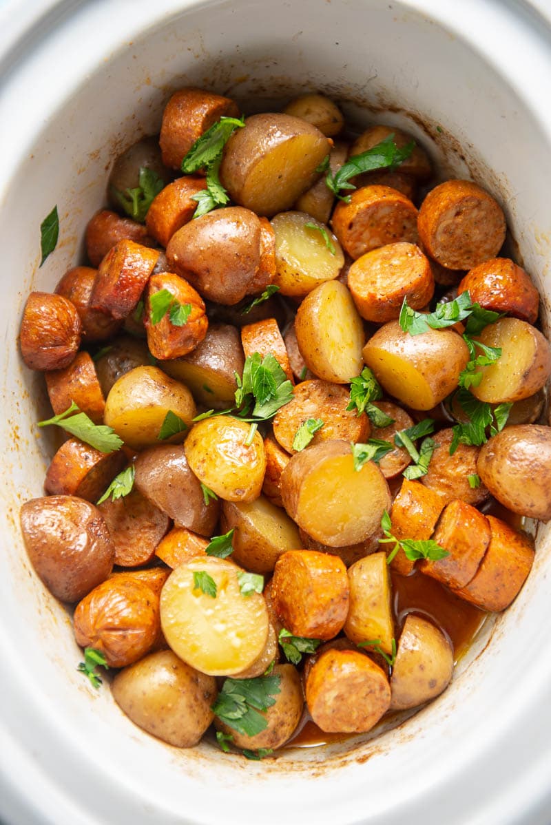 white oval slow cooker with sausage and potatoes