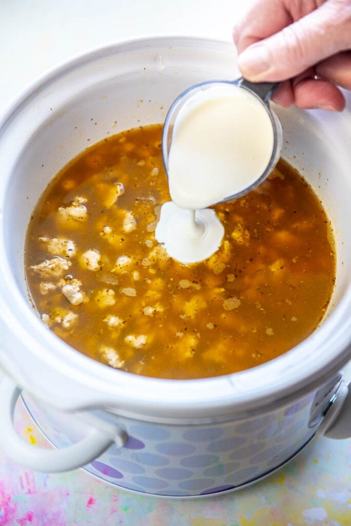 pouring cream in to white turkey chili in slow cooker