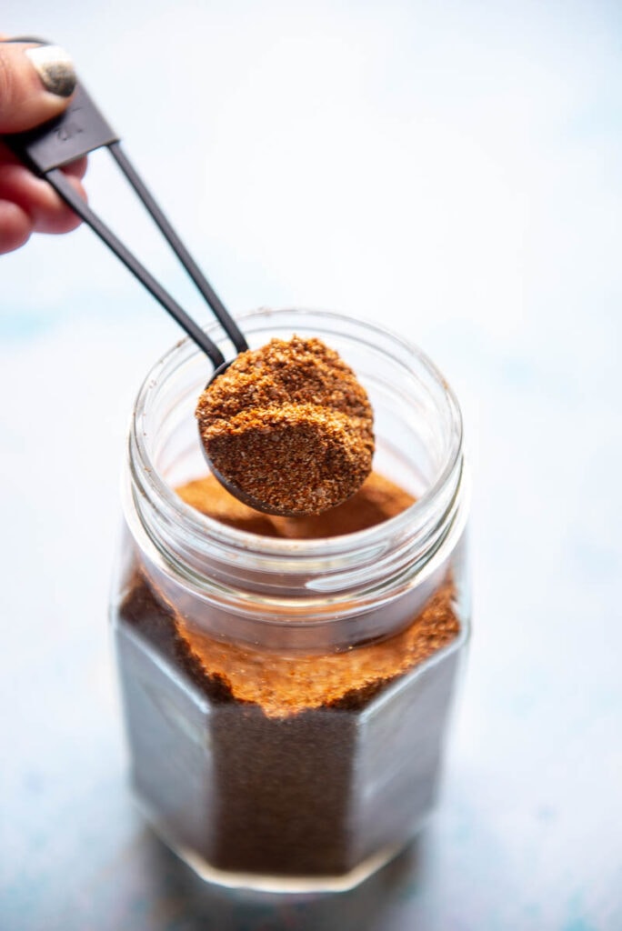 scooping a tablespoon of taco seasoning out of a glass jar