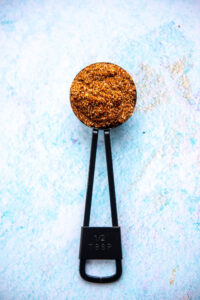 black tablespoon filled with taco seasoning on blue backdrop