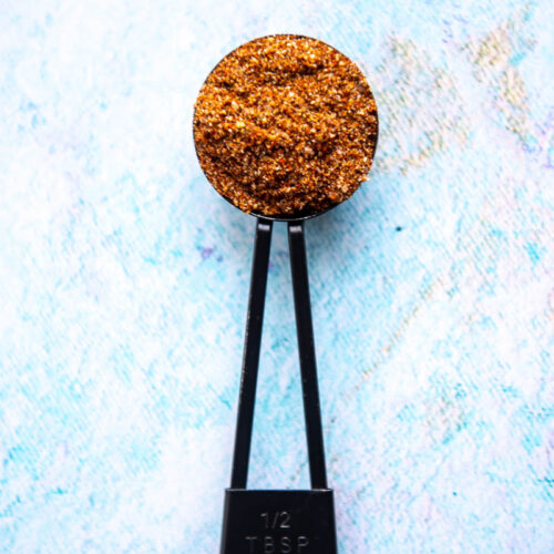 black tablespoon filled with taco seasoning on blue backdrop