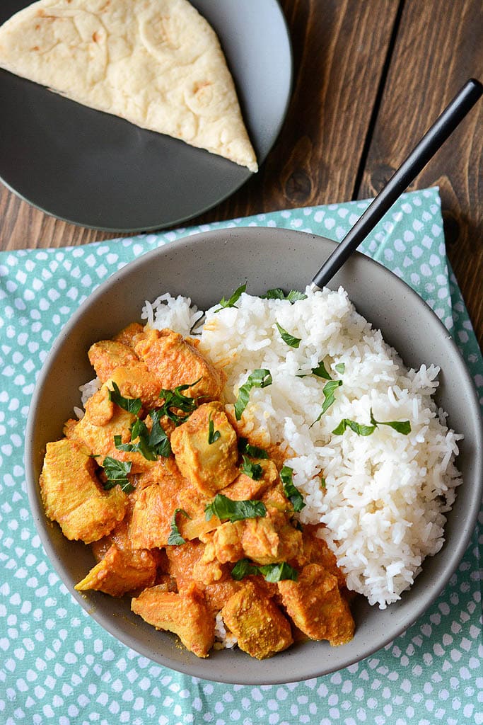 butter chicken in gray bowl with rice on green napkin