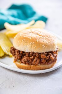 sloppy Joe with bun on white plate with pickles and chips