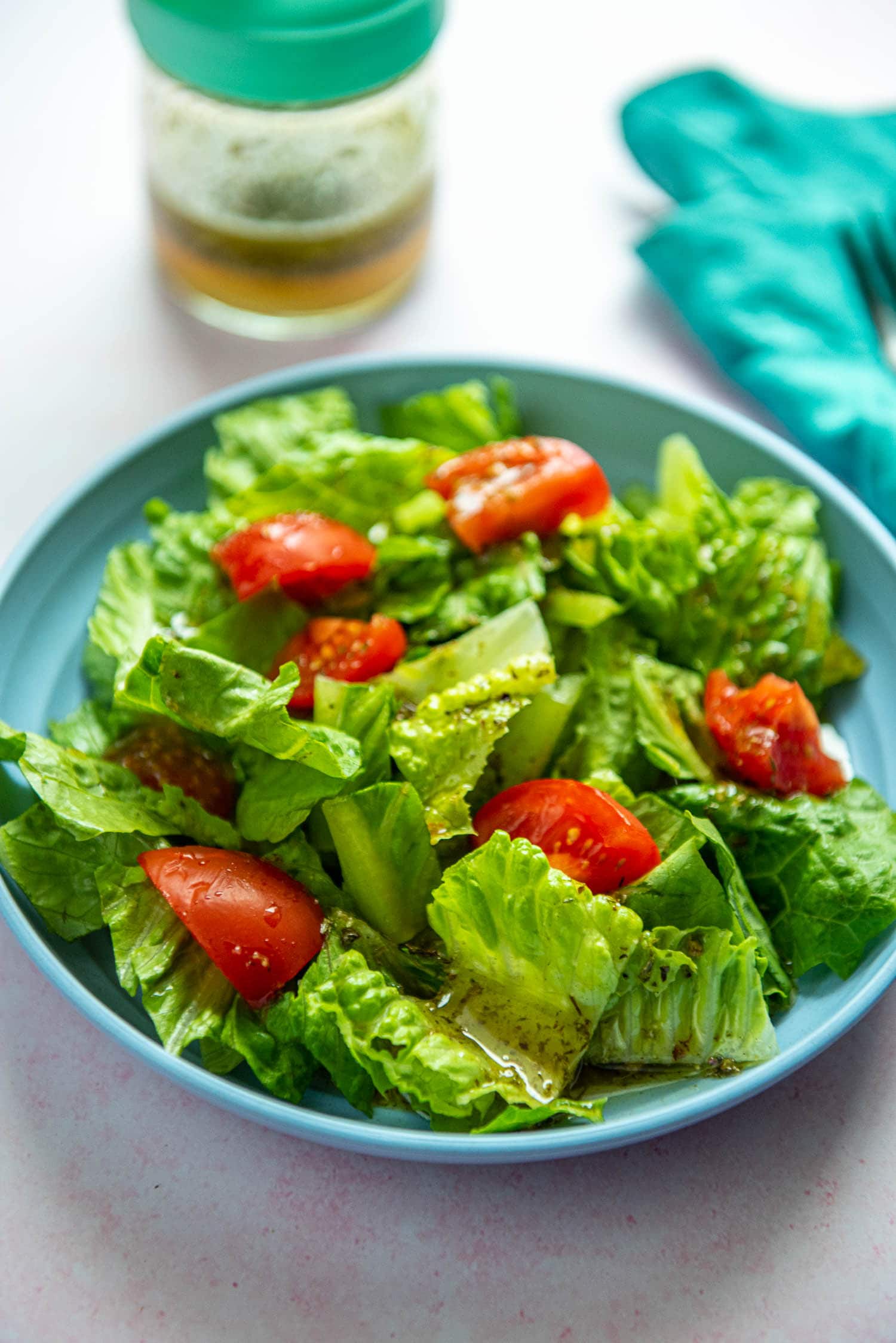 chopped romaine lettuce and chunks of tomato on blue plate with Italian dressing