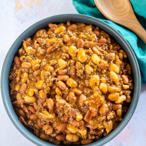 blue bowl of cowboy beans next to green napkin and wooden spoon