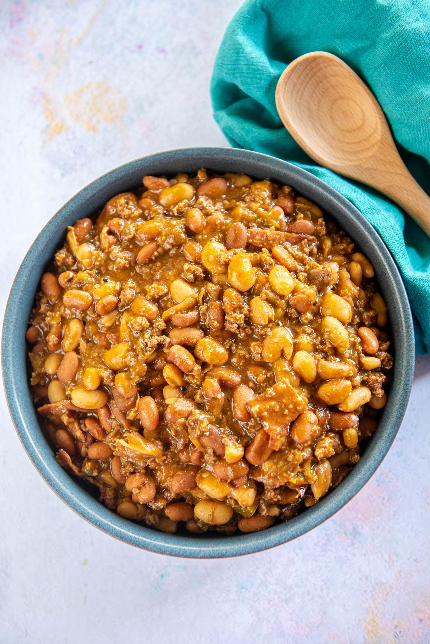 blue bowl of cowboy beans next to green napkin and wooden spoon