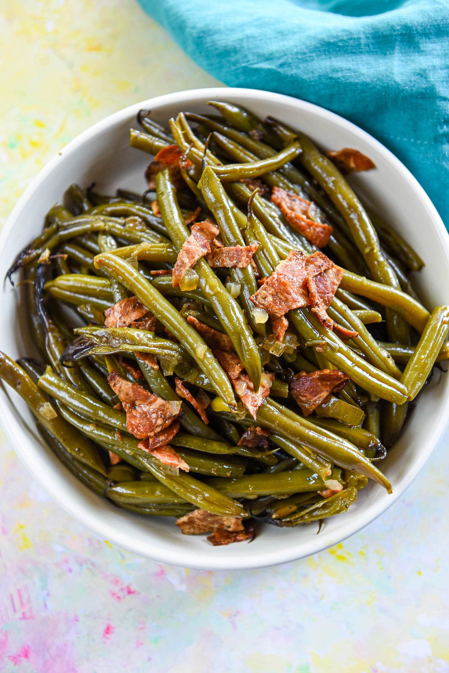cooked fresh green beans in white serving bowl topped with crispy bacon