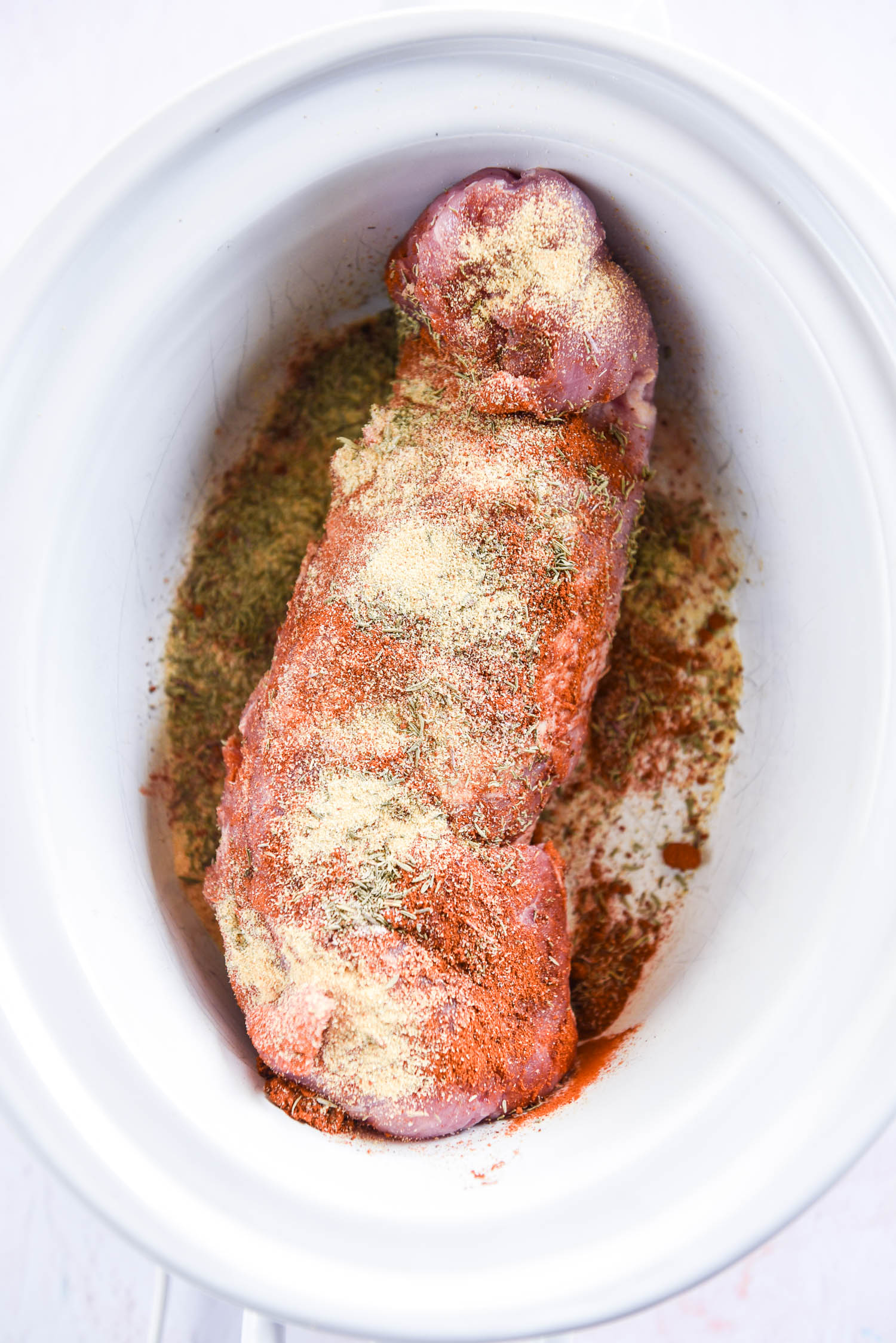 pork loin rubbed with seasonings ready to cook in white slow cooker